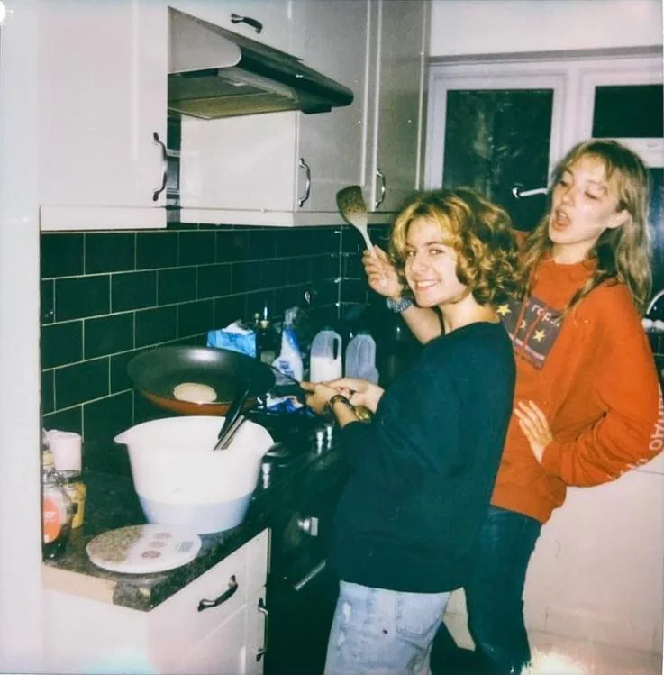 Two flatmates making pancakes together in a small kitchen at night.